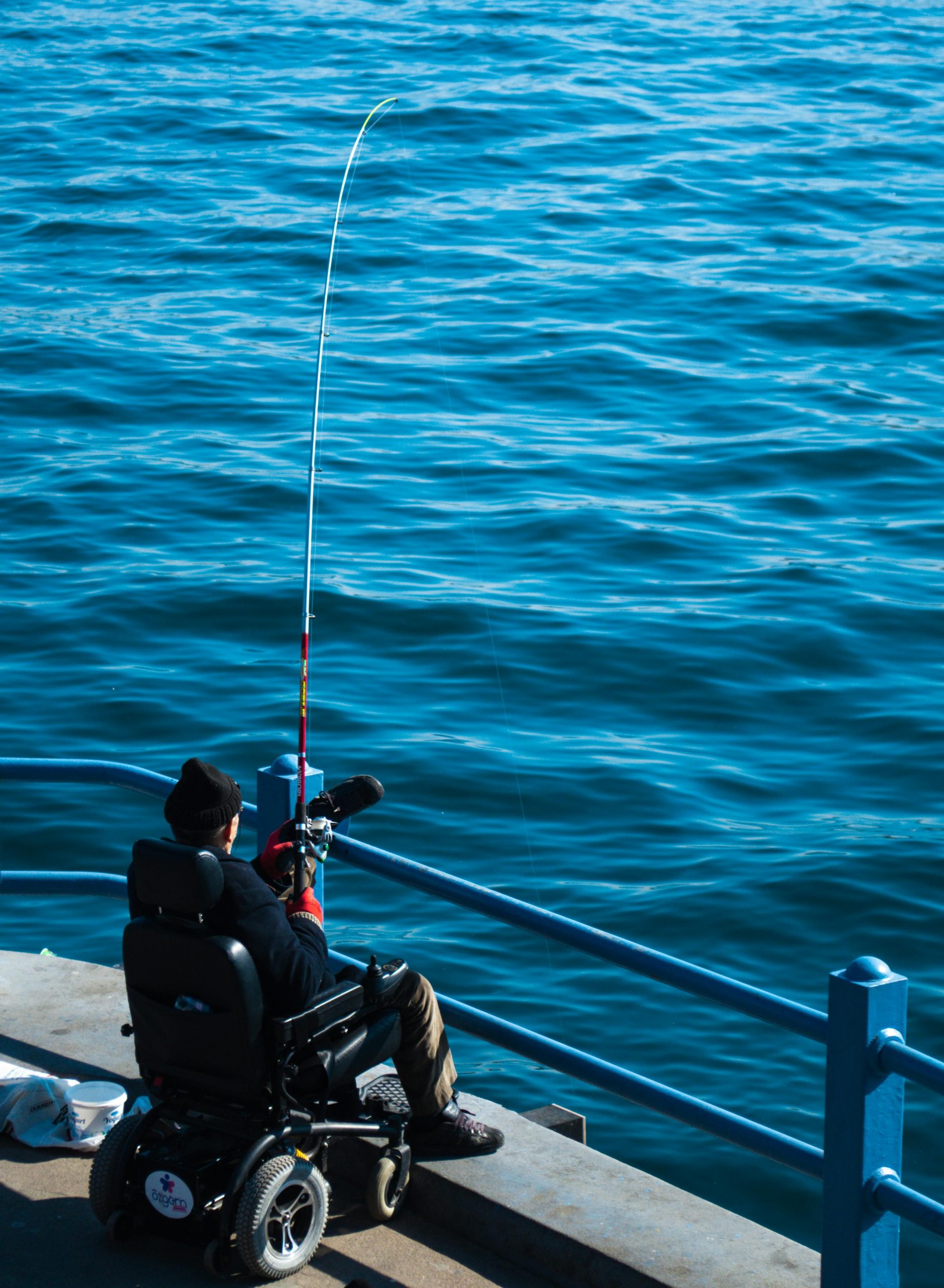 A person in a wheelchair fishing on a pier in Istanbul, Türkiye. Calm sea view.