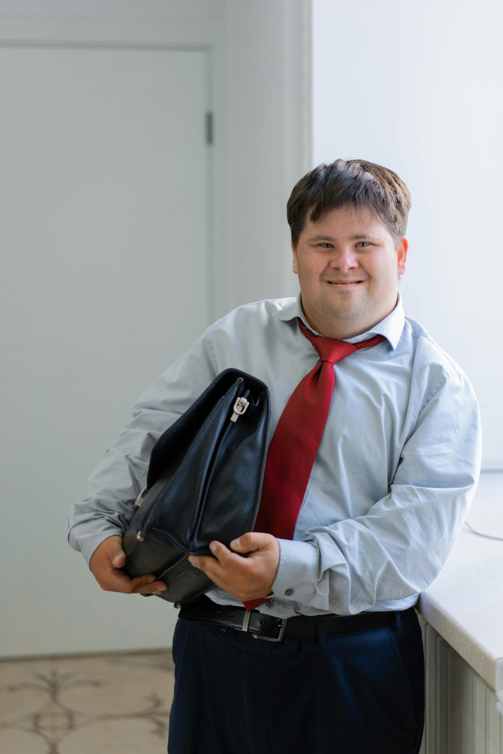 Confident businessman with Down syndrome holding a briefcase and smiling indoors.